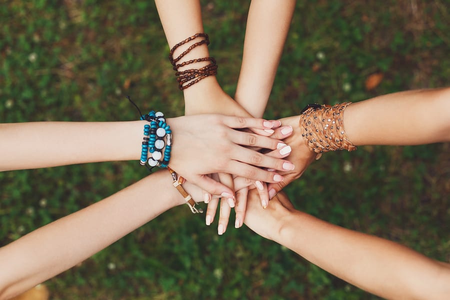 United hands of young females, top view. Stylish hands of girlfriends in boho hippie bracelets at green grass background. Togetherness and support, youth fashion and active lesiure. Women friendship